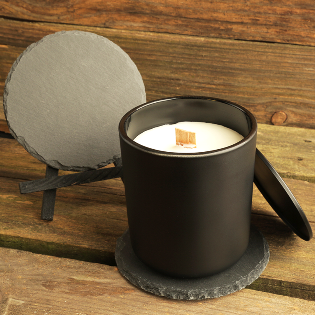 Black candle holder with a candle on a wooden surface, accompanied by a gray slate coaster and stand.