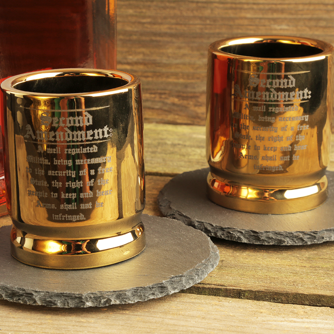 Two gold shot glasses with engraved text on a wooden surface.
