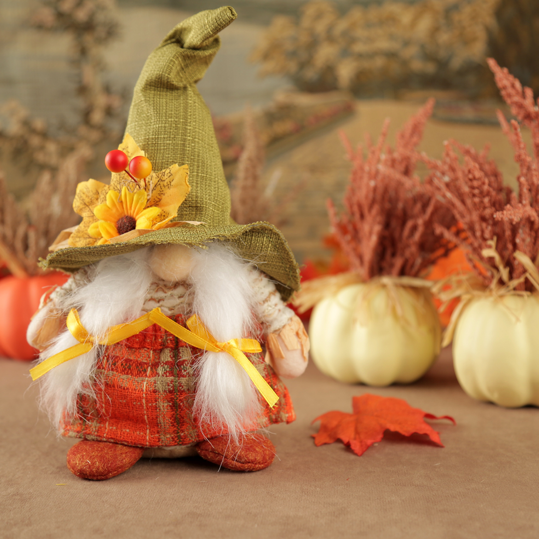 Decorative female gnome with a green hat and plaid outfit in a fall-themed setting with pumpkins and leaves.