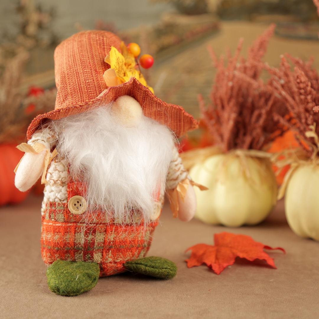 Autumn-themed male gnome figurine with plaid outfit and orange hat, surrounded by pumpkins and leaves.