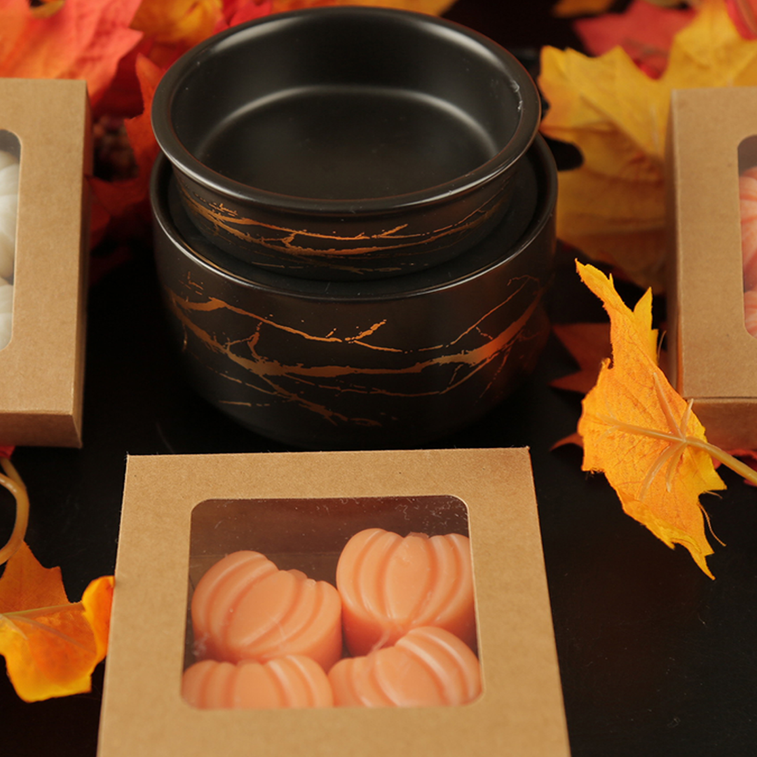 Black marble-patterned wax warmer with a box of wax melts on a dark surface with autumn leaves.