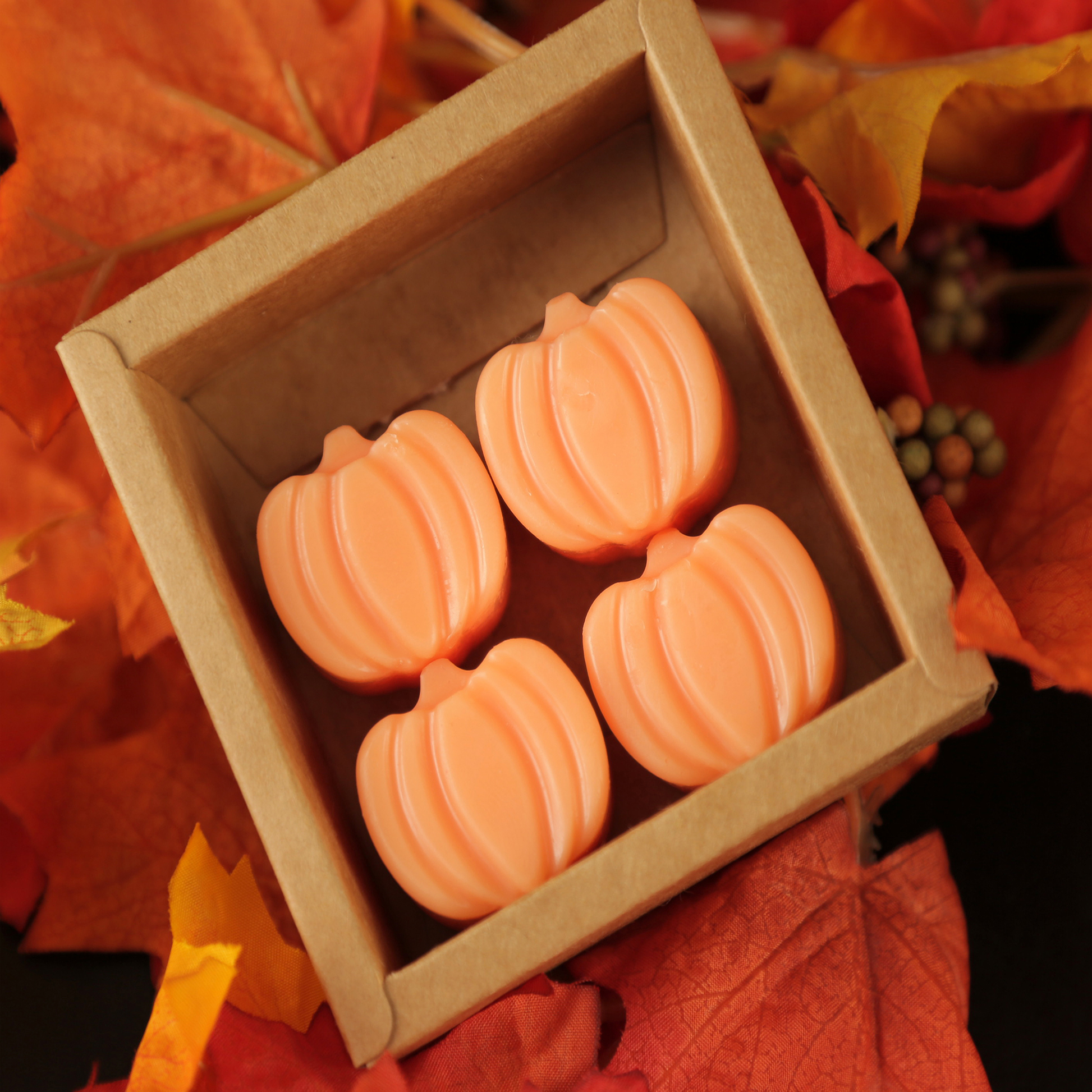 Four pumpkin-shaped soap bars in a box with autumn leaves in the background