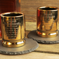 Two gold shot glasses with engraved text on a wooden surface.