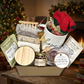 The Cozy Moments Gift Box combines bath and body treats with cozy comforts and tea-time favorites. It includes a herbal bath soak featuring Epsom salt, lavender, and roses, lavender soap, fluffy holiday socks, mini honey with a dipper, a gold coffee teaspoon, a thick glass 4 oz candle, a Hope mug, an exfoliating soap pouch, a bamboo wood soap holder, and two flavorful teas.
