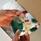 A person's hands holding a small Christmas-themed fuzzy sock gift box with a gold ribbon bow, set against a Christmas gift box.