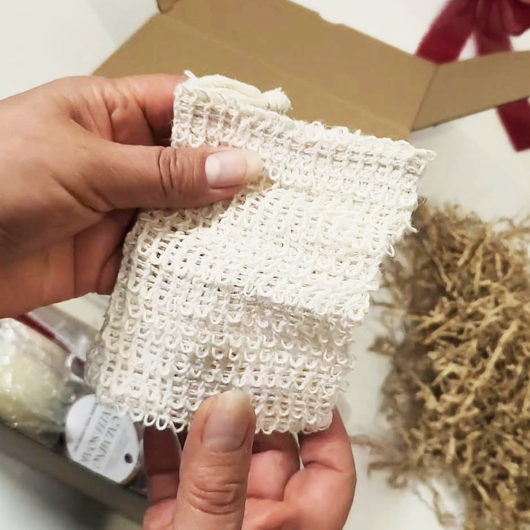 A close-up of a hand holding a small Exfoliating Soap Pouch for Bath & Shower.  The Cozy Moments Gift Box