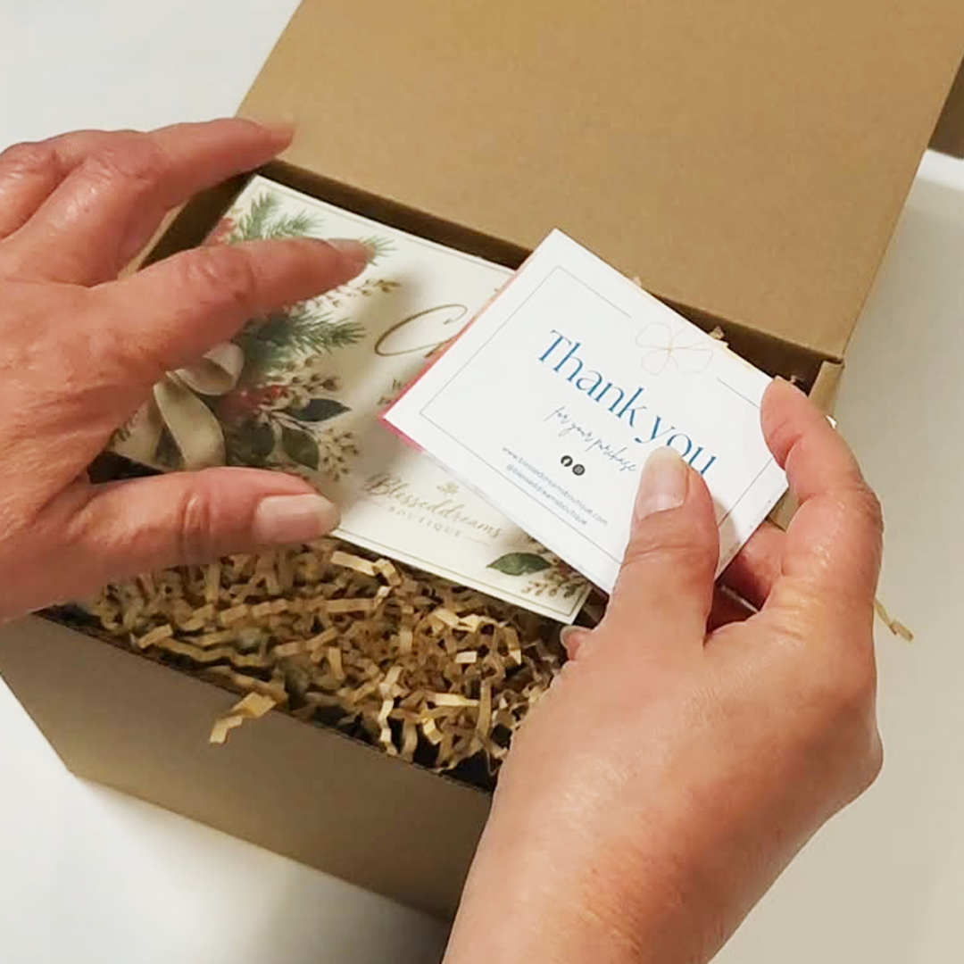 A person's hands holding a 'Thank you' card above The Cozy Sips Gift Box.