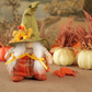 Decorative female gnome with a green hat and plaid outfit in a fall-themed setting with pumpkins and leaves.