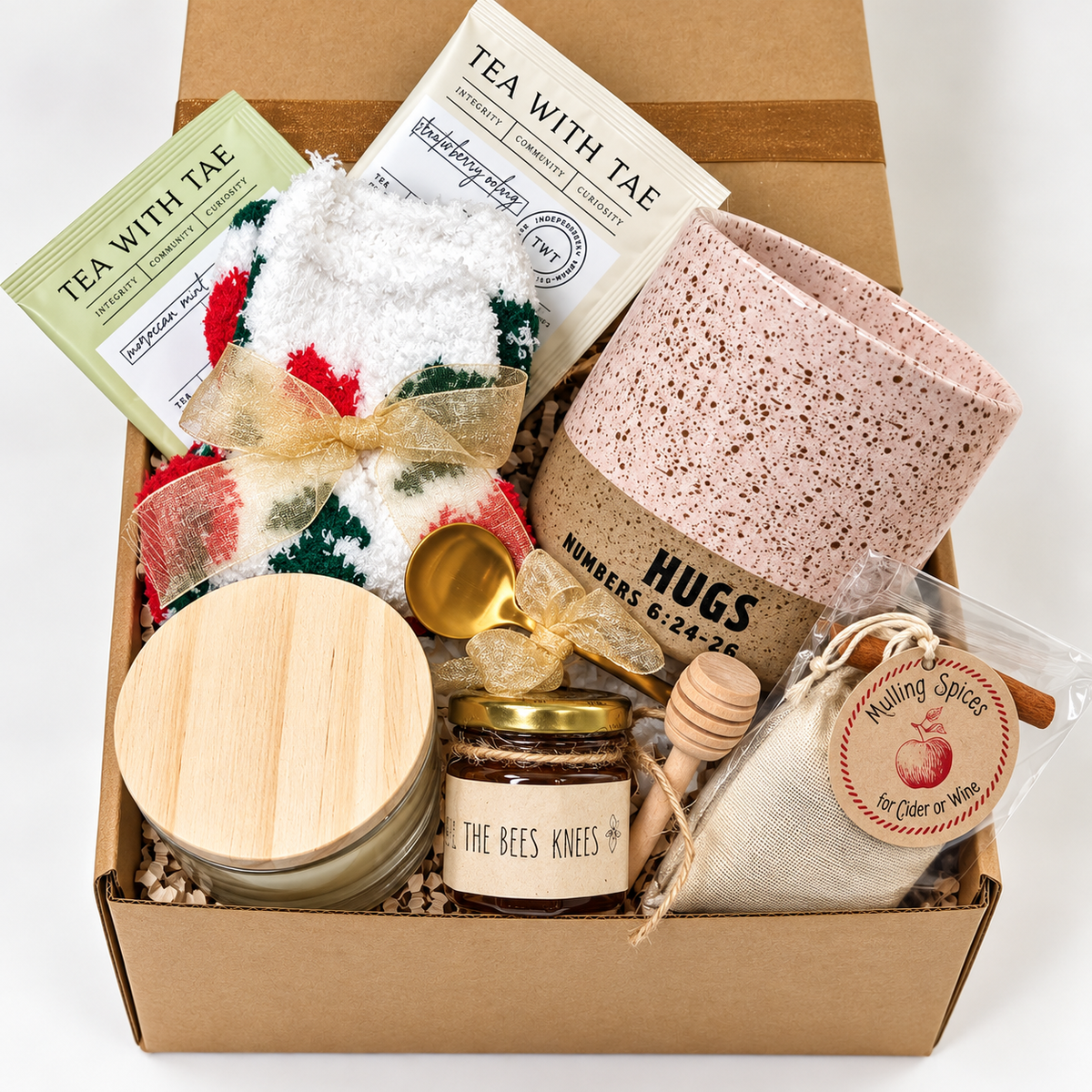 The Cozy Sips Gift Box combines the cozy comforts of tea-time favorites. It includes a Hug Mug, fluffy holiday socks, mini honey with a dipper, a gold coffee teaspoon, a hand-poured 4 oz candle, two flavorful teas and Mulling Spices.
