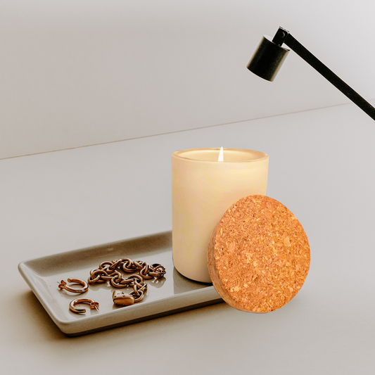 A lit cream-colored candle in a matte vessel sits on a cream stoneware tray with a Candle Snuffer.