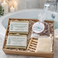 Bath gift set with soaps, bath salts, and a scrubber in a box on a bathroom counter.