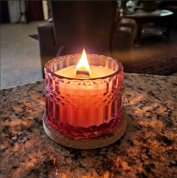 A pink glass candle jar sits on a stack of natural wood slices, surrounded by a wooden bead garland, tassel decor,  in front of a mirror. 
Heavenly Chocolate Cherries-7oz posh candle vessel & lid - translucent mauve__al3