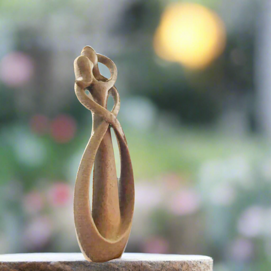 An abstract resin sculpture of a kissing couple, with a blurred background featuring bokeh lights and a plant.