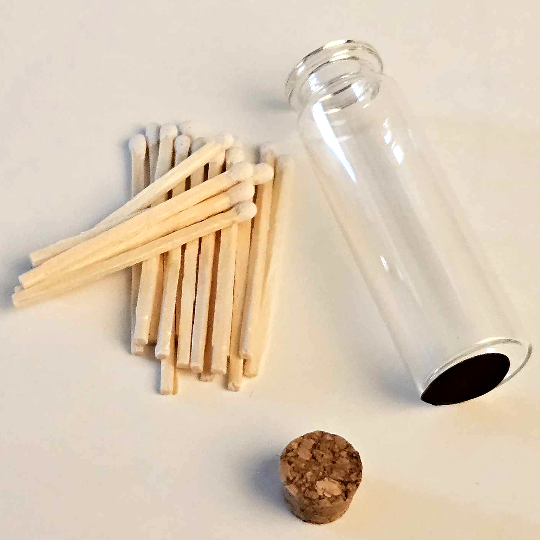 A clear glass vial with a cork stopper, shown next to a small pile of wooden matchsticks on a plain light background.
