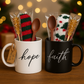 Two mugs, one white and one black, with 'hope' and 'faith' text, containing Christmas-themed items.