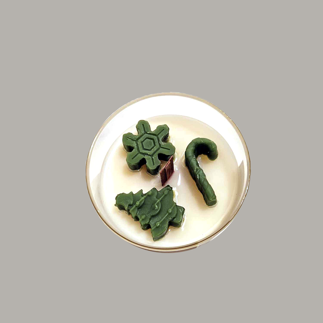 Yuletide Bliss - Wood Wick Soy Candle with green tree, cane and snowflake christmas decor on top of the candle.