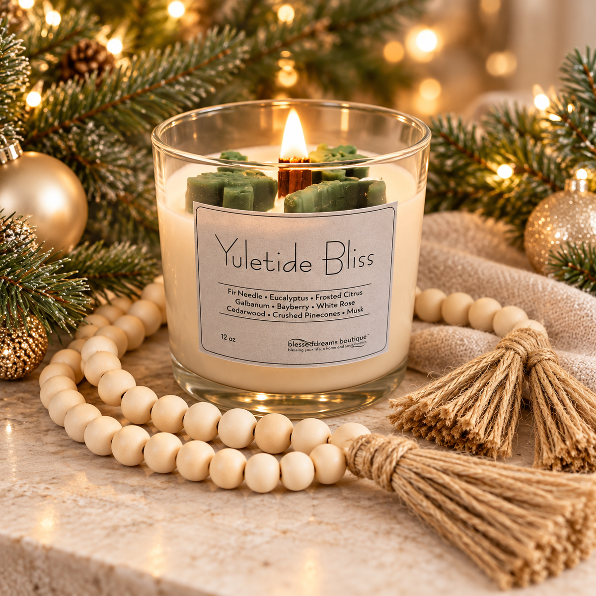 A lit candle in a clear glass jar labeled 'Yuletide Bliss' styled with wooden beads, tassel cords, pine branches, and warm holiday lights on a stone surface.