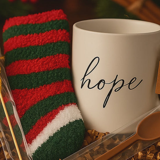 White mug with 'hope' text, red and green striped socks, chocolate spoon, and a sugar stick candy in a gift box.