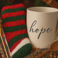 White mug with 'hope' text, red and green striped socks, chocolate spoon, and a sugar stick candy in a gift box.